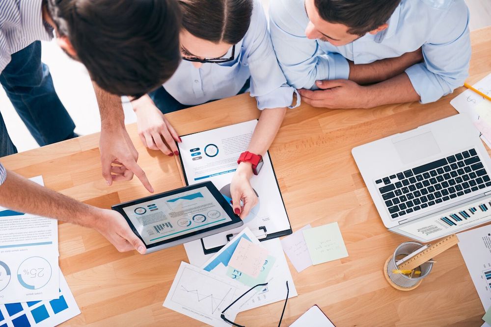 Three people looking at some charts on a tablet